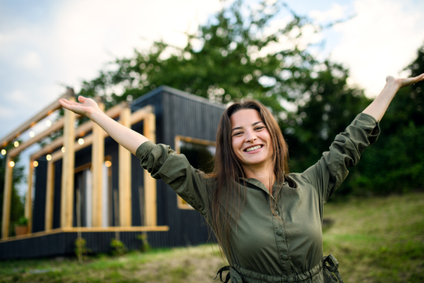 Young woman looking at camera outdoors, weekend away in container house in countryside.