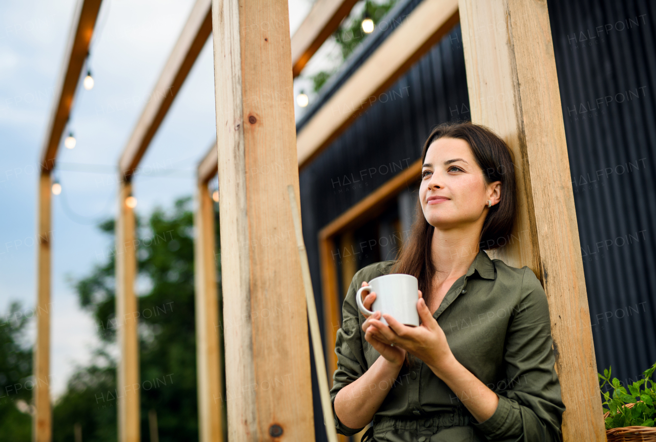 Young woman with coffee outdoors, weekend away in container house in countryside.