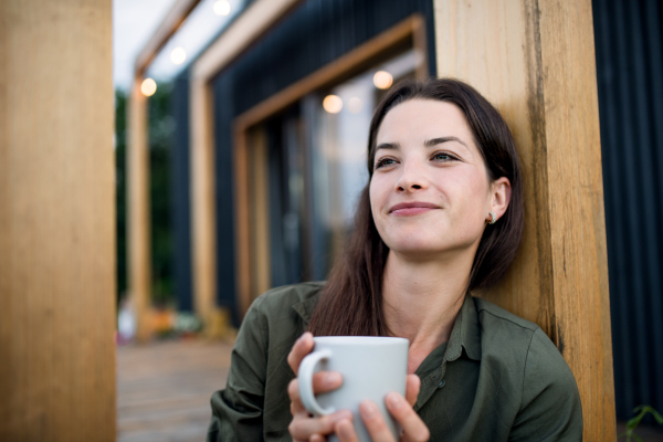 Portrait of young woman with coffee outdoors, weekend away in container house in countryside.