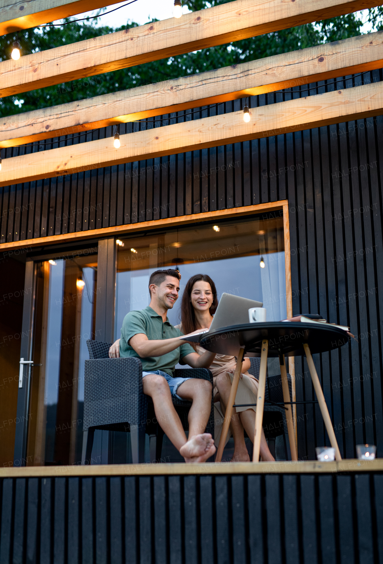 Young couple with laptop sitting outdoors, weekend away in container house in countryside.