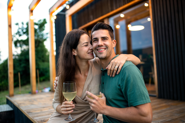 Young couple with wine sitting outdoors, weekend away in container house in countryside.