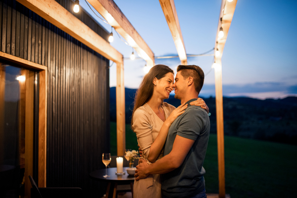 Happy young couple dancing outdoors at dusk, weekend away in container house in countryside.