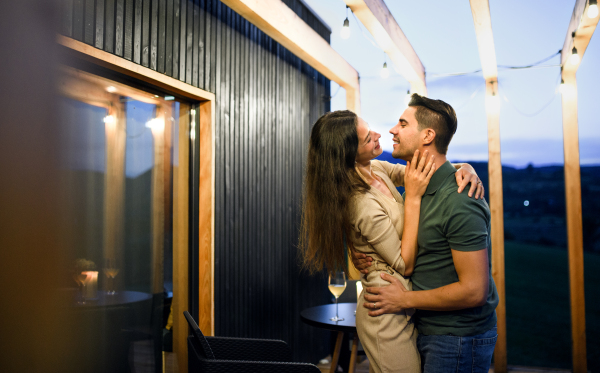 Happy young couple dancing outdoors at dusk, weekend away in container house in countryside.