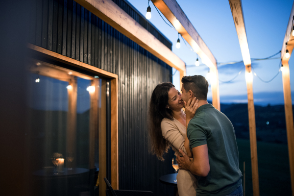 Happy young couple dancing outdoors at dusk, weekend away in container house in countryside.