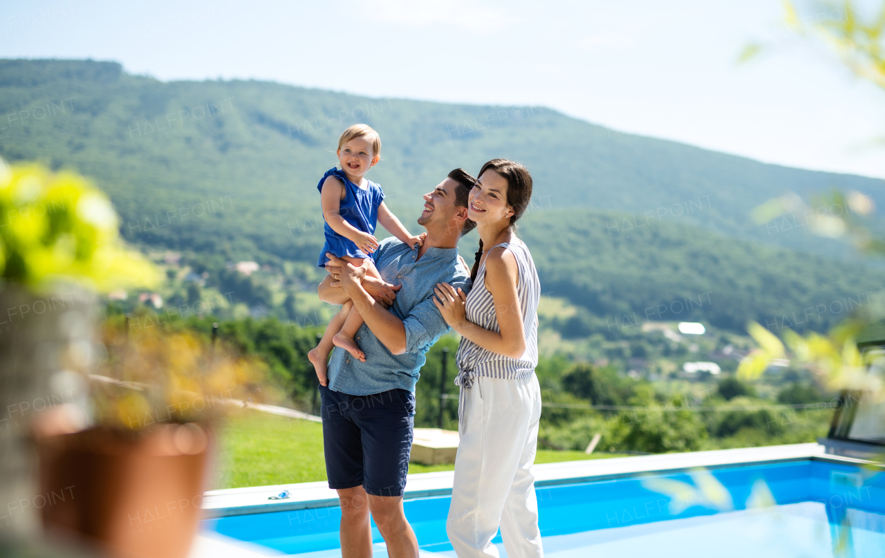 Portrait of young family with small daughter outdoors in backyard garden, relaxing.