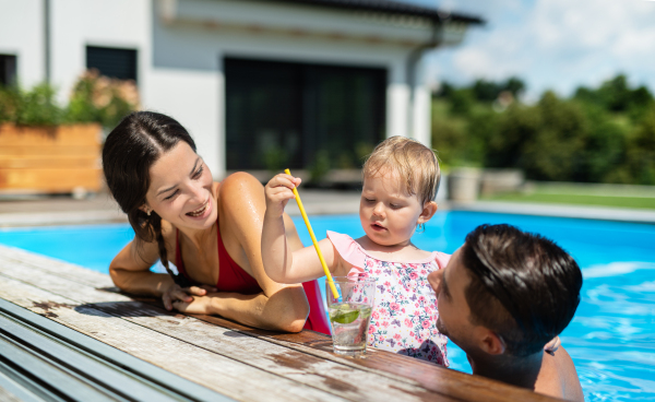 Happy young family with small daughter in swimming pool outdoors in backyard garden.