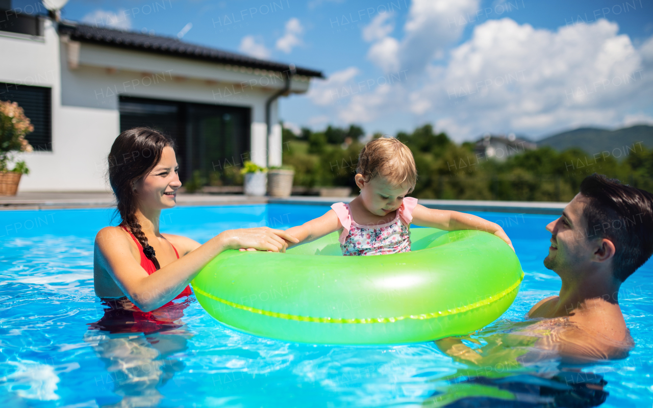 Happy young family with small daughter in swimming pool outdoors in backyard garden.