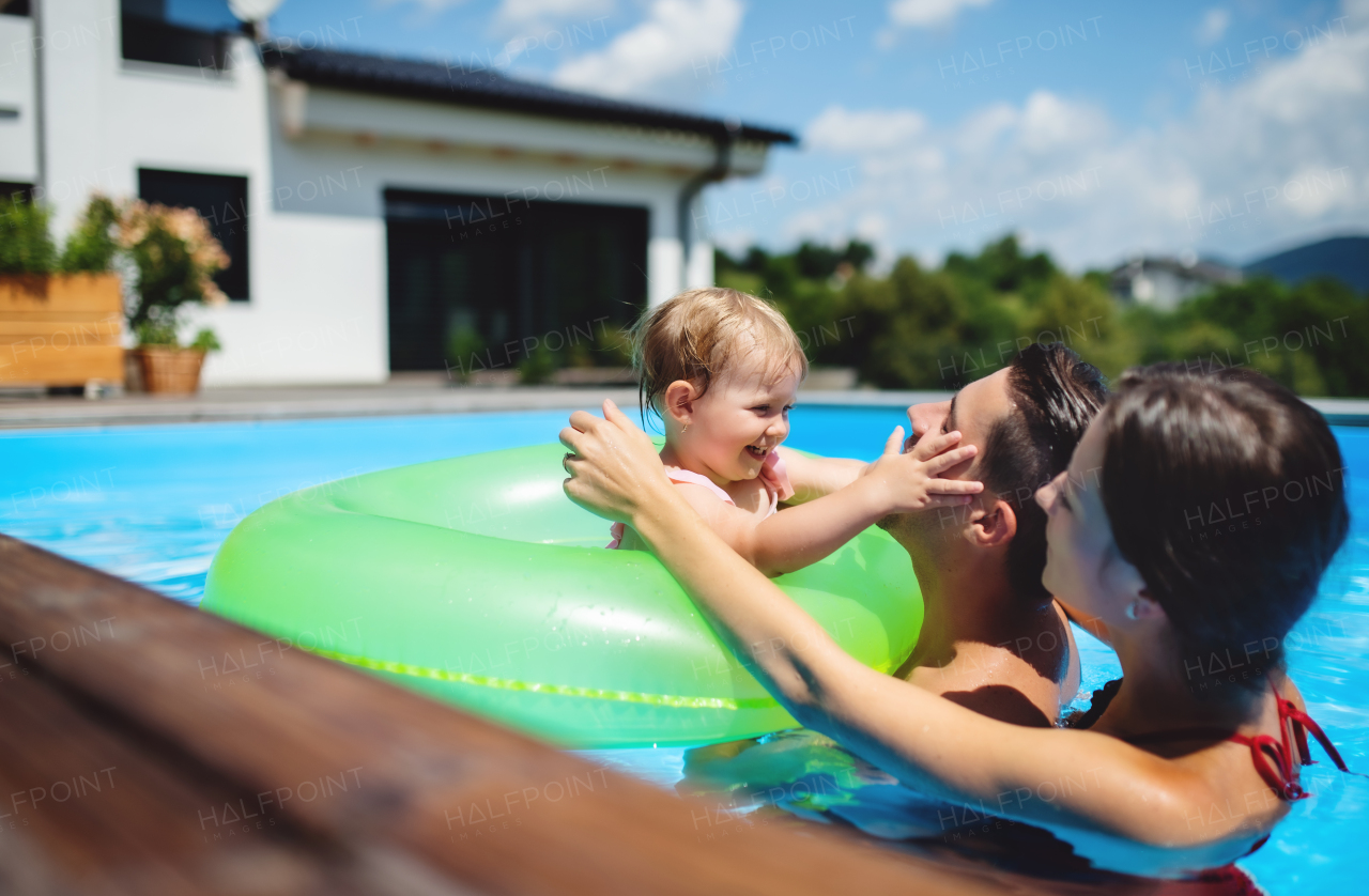 Happy young family with small daughter in swimming pool outdoors in backyard garden.