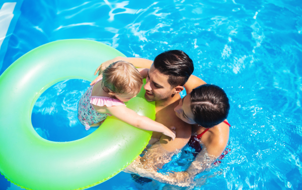 Top view of young family with small daughter in swimming pool outdoors in backyard garden.