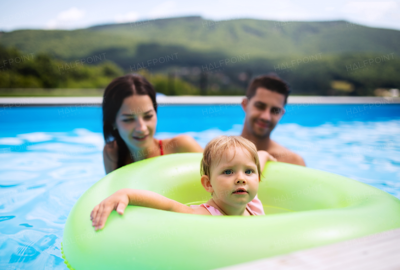 Happy young family with small daughter in swimming pool outdoors in backyard garden.