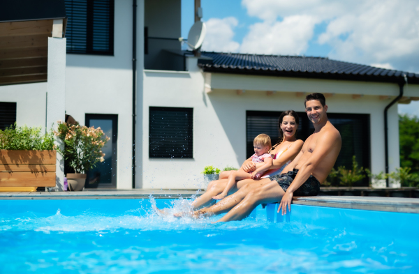 Happy young family with small daughter in swimming pool outdoors in backyard garden.