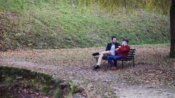 Senior father and his young son sitting on bench in nature, talking.