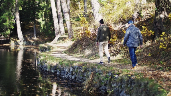 Rearview of senior father and his young son walking by lake in nature, talking.