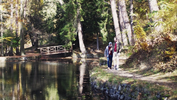 Senior father and his young son walking by lake in nature, talking.