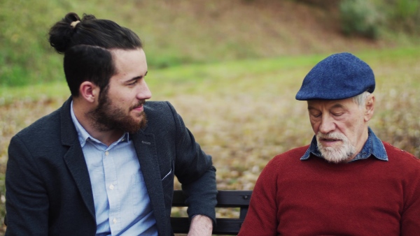 Senior father and his young son sitting on bench in nature, talking.