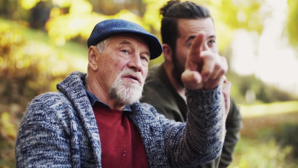 Senior father and his young son sitting on bench in nature, talking and eating.