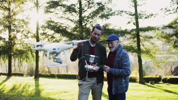 Senior father and his young son with drone in nature, talking.