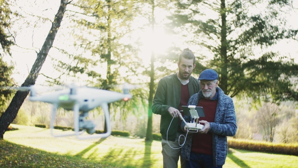 Senior father and his young son with drone in nature, talking.