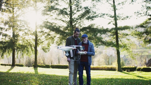 Senior father and his young son with drone in nature, talking.