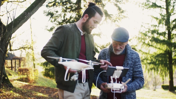 Senior father and his young son with drone in nature, talking.