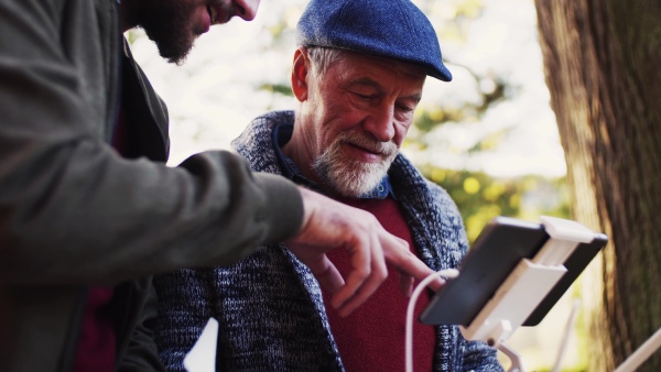 Senior father and his young son with drone in nature, talking.