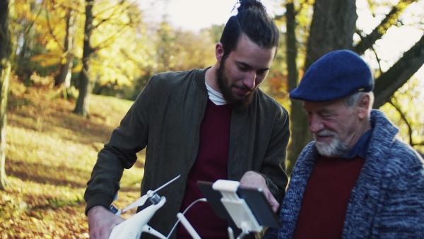 Senior father and his young son with drone in nature, talking.