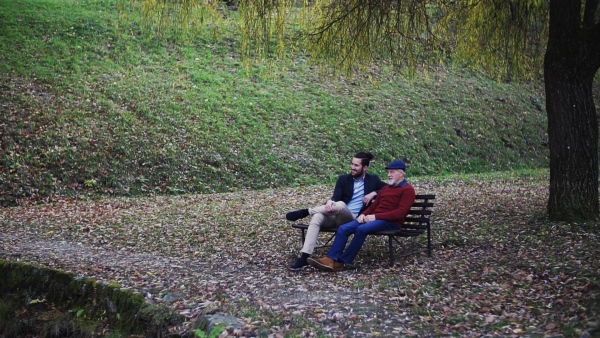 Senior father and his young son sitting on bench by lake in nature, talking. Slow motion.