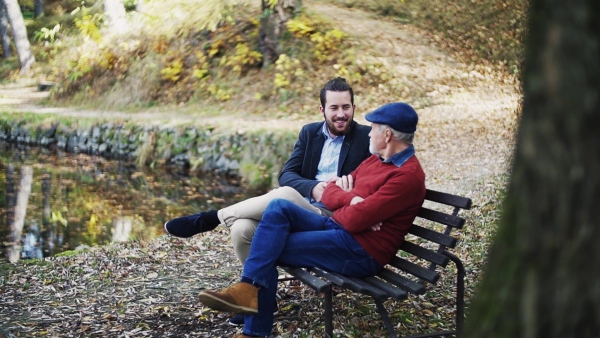 Senior father and his young son sitting on bench by lake in nature, talking. Slow motion.