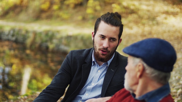 Senior father and his young son sitting on bench in nature, talking.