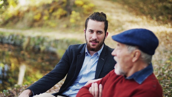 Senior father and his young son sitting on bench by lake in nature, talking. Slow motion.