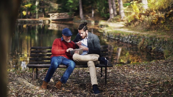 Senior father and his son sitting on bench in nature, using tablet. Slow motion.