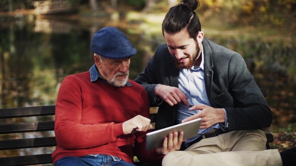 A senior father and his son sitting on bench in nature, using tablet and smartphone. Slow motion.