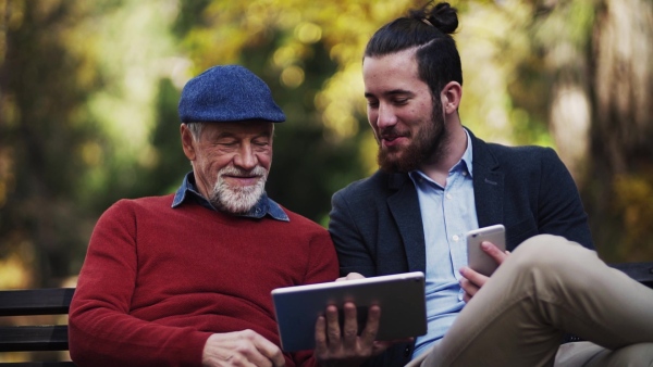 A senior father and his son sitting on bench in nature, using tablet and smartphone. Slow motion.