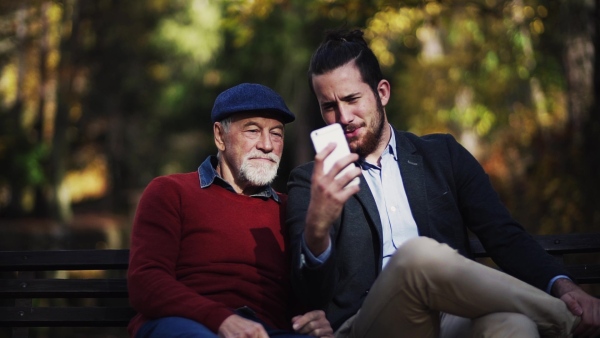 Senior father and his son with smartphone sitting on bench in nature, taking selfie. Slow motion.