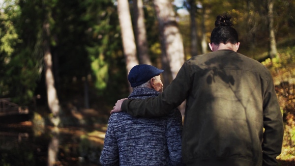 Rear view of senior father and his young son walking in nature, talking. Slow motion.