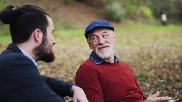 Senior father and his young son sitting on bench in nature, talking.