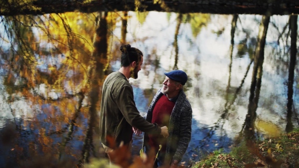 Senior father and his son standing by lake in nature, hugging. Slow motion.