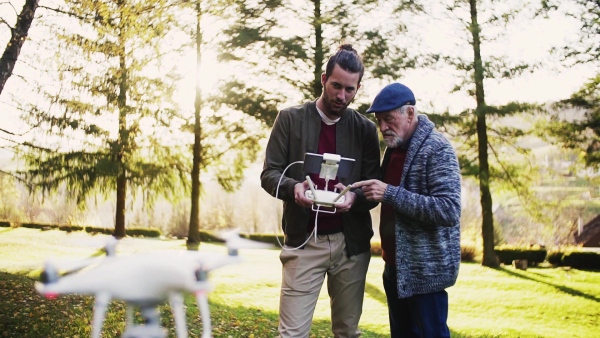 Senior father and his young son with drone in nature, talking. Slow motion.