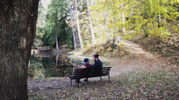 Rear view of senior father and his young son sitting on bench in nature, talking.