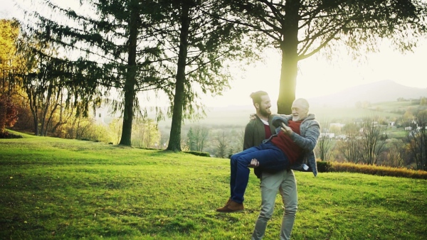 A young man carrying his senior father in arms in nature, spinning. Slow motion.