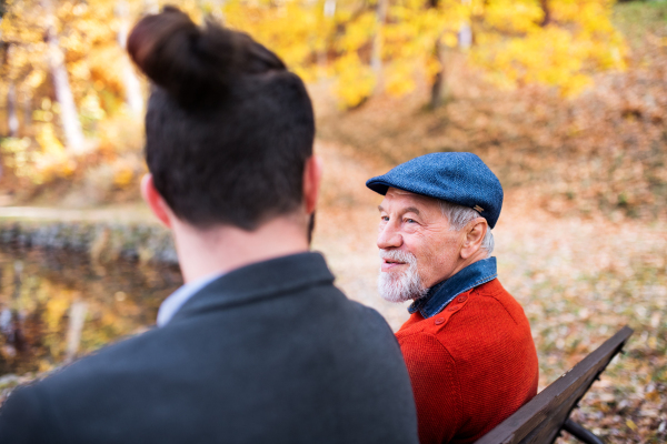 Senior father and his young son sitting on bench by lake in nature, talking.