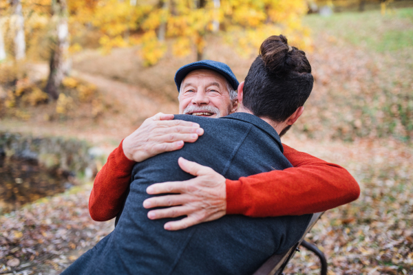 Senior father and his young son sitting on bench by lake in nature, hugging.