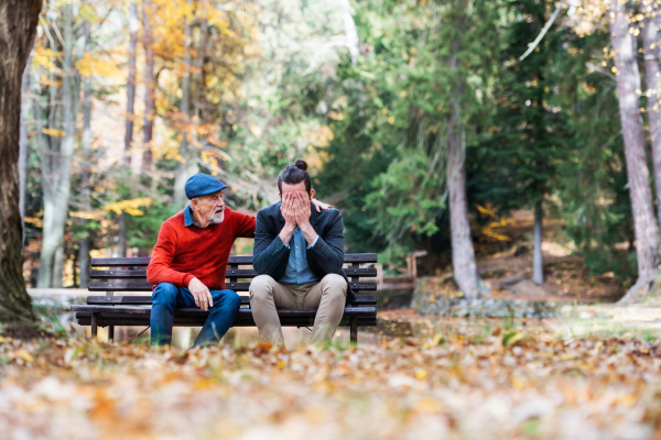 Senior father comforting his sad and frustrated adult son on bench in nature.