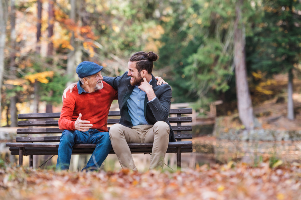 Senior father and his young son sitting on bench by lake in nature, talking.