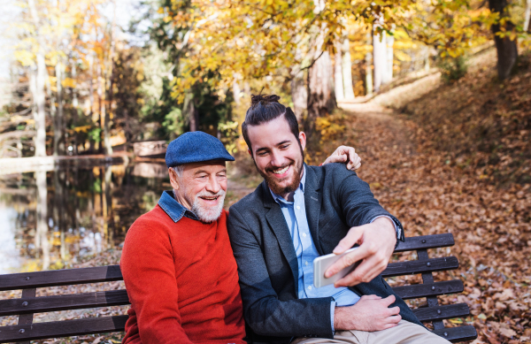 Senior father and his son with smartphone sitting on bench in nature, taking selfie.