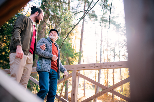 A senior father with walking stick and his son on walk in nature, talking.