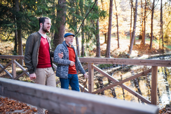 A senior father with walking stick and his son on walk in nature, talking.