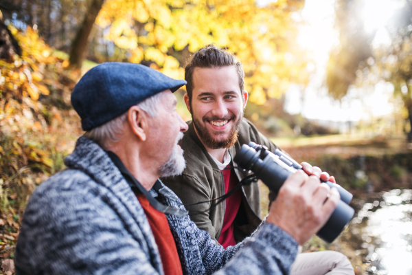 Senior father and his son with binoculars sitting on bench in nature, talking.