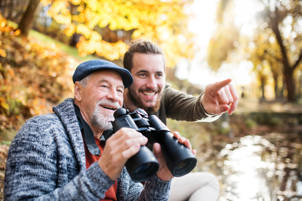 Senior father and his son with binoculars sitting on bench in nature, talking.