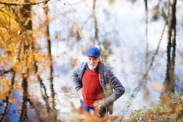 High angle view of lonely senior man standing by lake in nature, looking at camera.